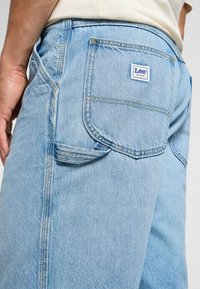 Jasnoniebieskie dżinsy z denimu z tylną kieszenią z logo "Lee"; widoczne szczegóły przeszycia i luźny krój.