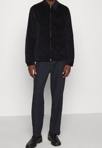 Giacca nera con zip, dalla texture liscia e colletto, abbinata a pantaloni blu navy e stivali neri. Design semplice e funzionale.