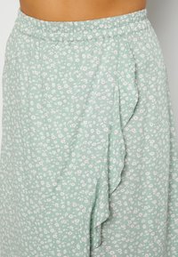 Lichtgroene rok met een klein wit en roze bloemenpatroon, elastische tailleband en ruches langs de zijnnaad.