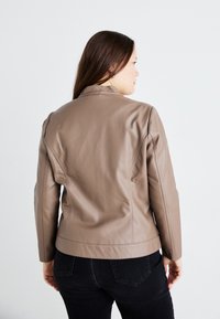 Chaqueta de cuero marrón con un diseño ajustado, hombros estructurados y una silueta elegante. Detalles de costura visibles a lo largo de las costuras.