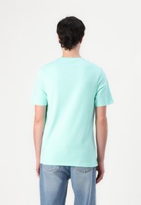T-shirt vert menthe à manches courtes, col rond, en coton doux. Design simple avec une texture lisse ; associé à un jean en denim bleu clair.