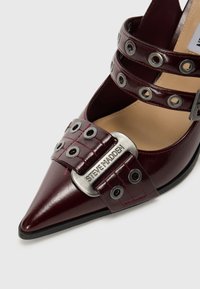 Bordo lakirani čizmi sa potpeticom i šiljastim vrhom, s više trakica, metalnim rupicama i srebrnom kopčom s ugraviranim "Steve Madden".