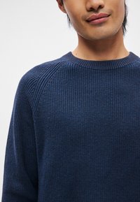 Pulover Navy din tricot cu striații, cu guler rotund și mâneci raglan. Prezintă un material texturat și o croială lejeră. Fără modele distincte sau accesorii.