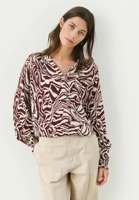 Garšīga piedurkņu blūze bordo un krēmkrāsas zebra rakst�ā, ar V formas dekoltē un elastīgu aproču, izgatavota no viegla auduma.