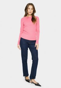 Skinny jeans van donkerblauwe denim, gecombineerd met een aansluitend, lang mouw ribbelshirt in levendig roze en zwarte slingback schoenen met puntige neuzen.