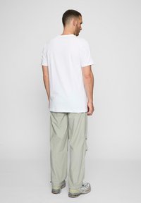 Hvid kortærmet T-shirt parret med lysegrå cargo-bukser. Bemærkelsesværdige detaljer inkluderer en afslappet pasform og minimalistisk design.