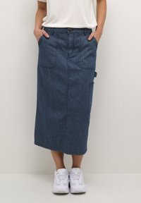 Falda midi de mezclilla en azul oscuro con corte recto, bolsillos delanteros y un bolsillo lateral. Combinada con zapatillas blancas.