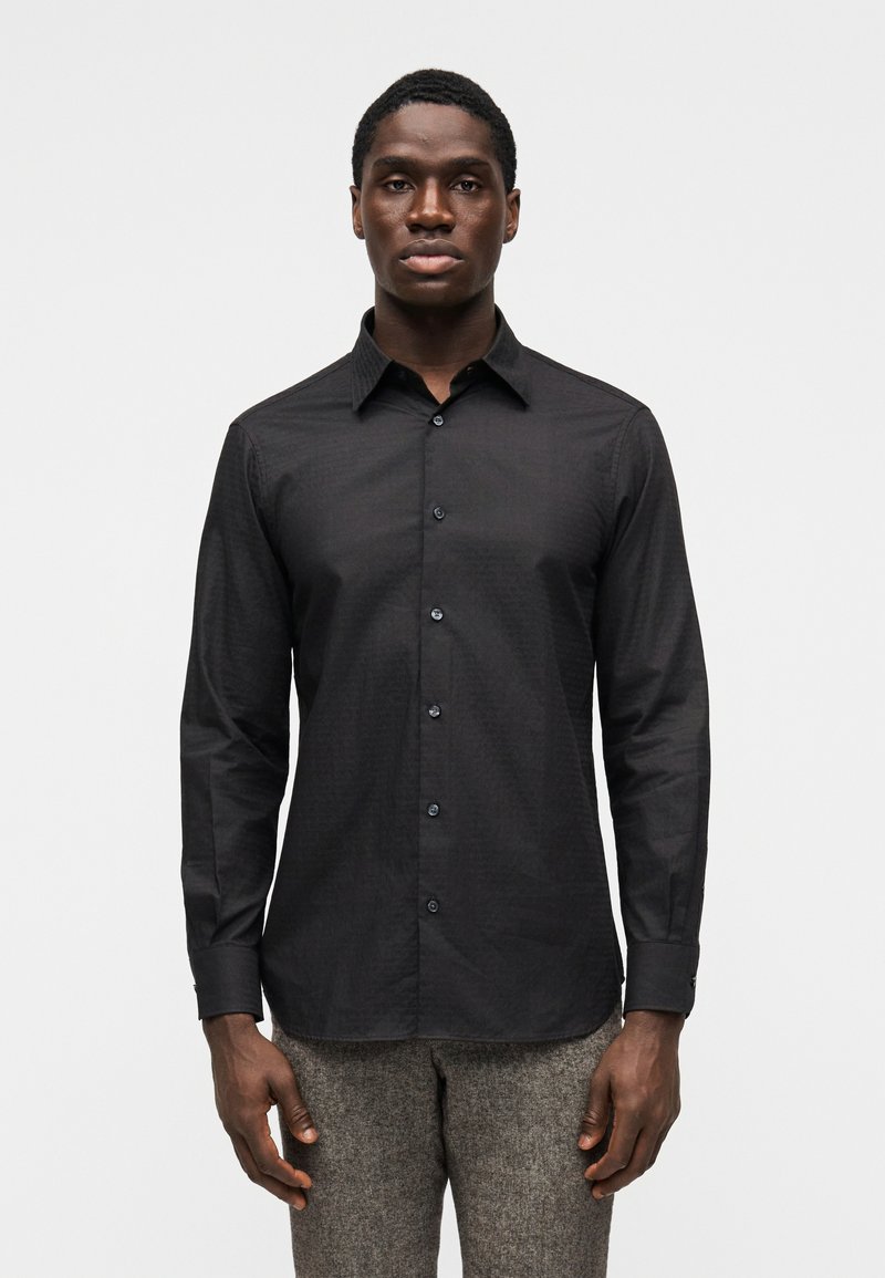 Camisa preta de botões com gola estruturada, mangas compridas e textura subtil. Fechada com botões escuros, desenhada para um ajuste personalizado.