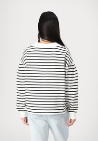 Svart og hvit stripete hettegenser med lange, voluminøse ermer og rund hals, kombinert med lys blå jeans. Myk bomullsmateriale.