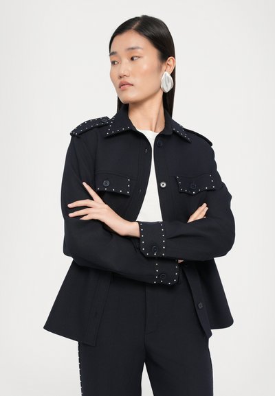 Navy jacket with a structured design, featuring studded accents on the collar and cuffs, two front pockets, and a buttoned closure.
