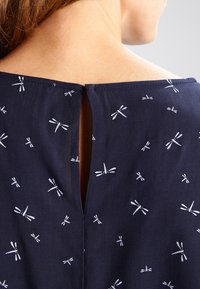 Námořnický top s klíčovou dírkou na zadní straně a opakovaným bílým vzorem vážky. Měkká textura, běžné střih a ležérní design.