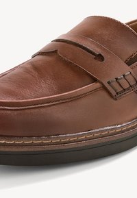 Mocassin en cuir marron avec couture moc toe, détail de bride penny et semelle en caoutchouc foncé sur fond blanc.