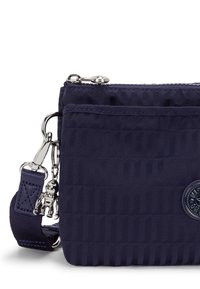 Borsa a tracolla in nylon blu marino con superficie testurizzata, accessori in argento, chiusura a zip e un ciondolo decorativo. Accento con logo circolare sul davanti.