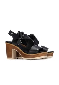 Sandalias de tacón alto de cuero negro con tiras cruzadas, detalles con tachuelas y suela plataforma en tono beige. Hebilla ajustable en el tobillo.
