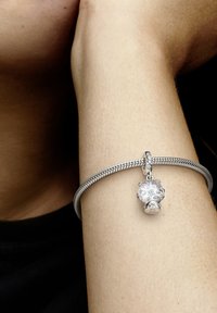 Srebrn zapestnica iz verižice z dekorativnim okrasom v obliki lobanje, z zapletenimi detajli in gladko površino.