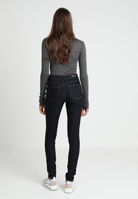 Černé skinny džíny s vysokým pasem, s zadními kapsami a nenápadnými švy, doplněné šedým topem s dlouhým rukávem a bílými teniskami.