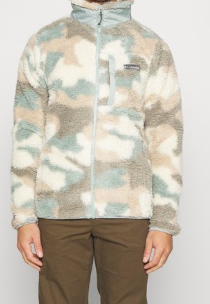 Fleecejack met lichtblauw, beige en wit camouflagepatroon, borstzak met rits en een volledige rits aan de voorkant, gedragen met een bruine broek.