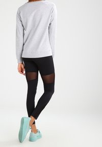 Sudadera gris de corte holgado, leggings negros con paneles de malla y zapatillas en azul claro con suelas texturizadas.
