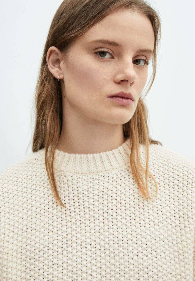 Pull en maille beige clair avec un col côtelé, présentant un motif texturé et un fil doux et épais. Détails subtils autour du col.