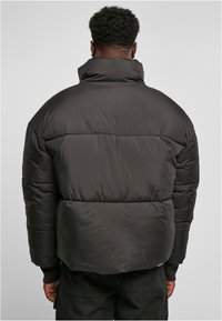 Chaqueta acolchada en negro mate, con un alto cuello y un diseño acolchado. Cuenta con una forma cuadrada y puños de canalé para mayor calidez.