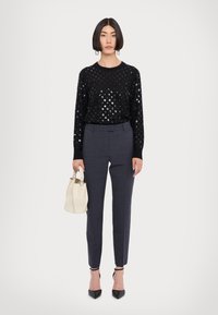 Μαύρο πουλόβερ με μεταλλικές βούλες, γκρι κομμένα παντελόνια και λευκή τσάντα κουβά. Μαύρες μυτερές γόβες ολοκληρώνουν την εμφάνιση.