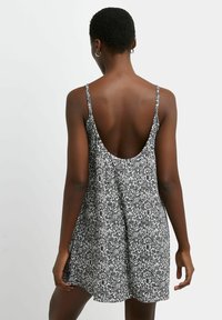 Mustavalkoinen kukkakuosiset mekko, jossa on ohuet olkaimet ja matala selkäosa, valmistettu kevyestä kankaasta, ja siinä on virtaviivainen siluetti.