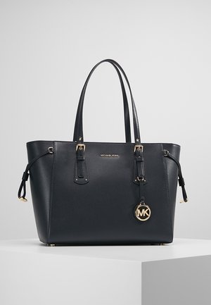 Sort tote taske med tekstureret faux læder, hardware i guldtoner, dobbelte top håndtag og et MK-logo charme hængende fra en sidelasse.