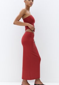 Robe rouge sans bretelles avec un corsage ajusté et une longue jupe avec un détail de fronces sur le côté, fabriquée à partir d'un tissu lisse et extensible.