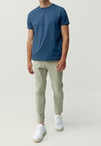 Blå bomullströja med rund hals och korta ärmar, kombinerad med ljusgröna slim-fit byxor och vita sneakers. Inga synliga mönster.