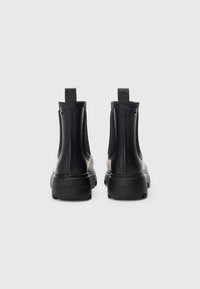 Black rubber ankle boots with elastic side panels, textured soles, and pull tabs, featuring a logo detail on the back.