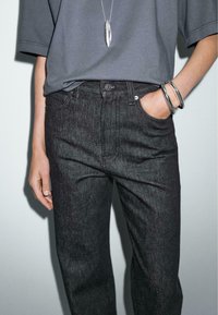 Jeans in denim scuro con una trama sottile, vita alta e design classico a cinque tasche. Indossata una t-shirt grigia oversize e una collana con pendente argentato.