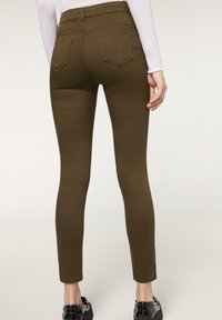Jeans skinny de color verde oliva con una cintura de tiro medio y bolsillos traseros, con una tela suave y elástica y una silueta ajustada hasta los tobillos.