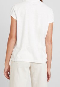 Camiseta blanca de manga corta con mangas enrolladas, fabricada en un tejido ligero, con un escote redondo y un corte holgado.