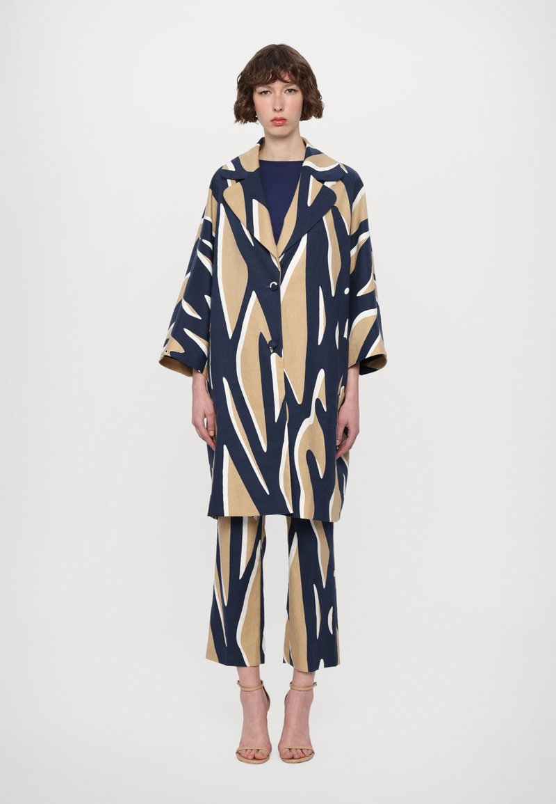 Navy and beige patterned coat with bold, abstract designs, paired with matching wide-leg pants. Fabric appears textured with a structured fit.
