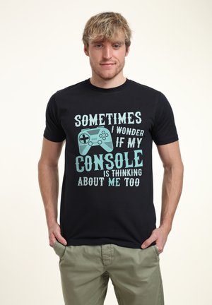 Sort t-shirt i sort bomuldsstof med lyseblå tekst: "Nogle gange spekulerer jeg på, om min spillekonsol også tænker på mig," med grafik af en spillekontrol.