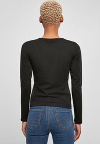 Schwarzes Langarmoberteil aus weichem Stoff, mit Rundhalsausschnitt und figurbetontem Design, kombiniert mit blauen Denim-Jeans mit Gesäßtaschen.