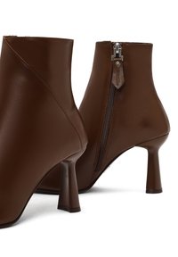 Bottines en cuir marron avec un bout pointu et un talon fin, dotées d'une fermeture éclair visible et d'une texture lisse.