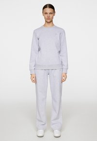 Ljusgrå bomullströja och matchande sweatpants. Enkelt design med manschetter vid handlederna och vristerna. Discret logotyp på bröstet och benet.