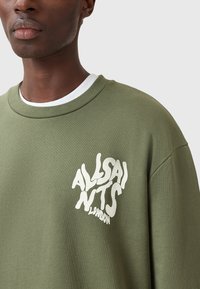 Felpa verde oliva con collo rotondo, caratterizzata da un logo grafico bianco sovradimensionato e testurizzato sul lato sinistro del petto. Materiale in cotone, vestibilità rilassata.