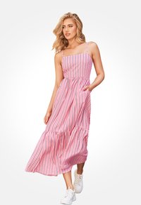 Roze en witte gestreepte maxi-jurk met dunne schouderbandjes, een gecinchte taille en een tiered rok. Draagt met witte sneakers.