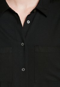 Zwarte overhemd met knoopsluiting van zachte stof, met twee voorzakken, een standaardkraag en metalen knopen met vier gaten.