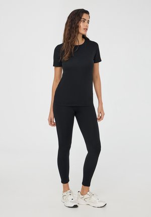 Top nero a maniche corte e leggings in tessuto elasticizzato, abbinati a scarpe da ginnastica bianche. L'outfit ha un design aderente e una texture liscia.