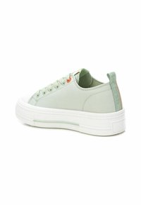 Zapatilla de lona verde claro con suela de goma blanca, atada con cordones verdes, que presenta un ojal naranja y una lengüeta trasera texturizada.