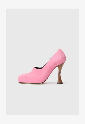 Zapato de tacón alto de ante rosa con puntera redondeada y tacón de madera curvado. Textura suave con un diseño de corte bajo en la parte frontal.