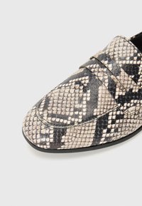 Mocassins en peau de serpent avec un motif noir et beige, une texture lisse et un bout arrondi. Deux bretelles décoratives sur le dessus.