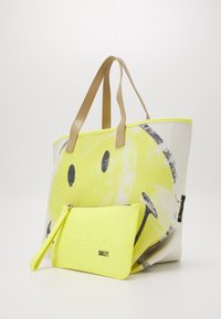 Duża torba tote z teksturowanym siateczkowym wykończeniem, z żółtym wzorem uśmiechniętej twarzy, karmelowymi uchwytami oraz zdejmowaną neonową saszetką z logo.