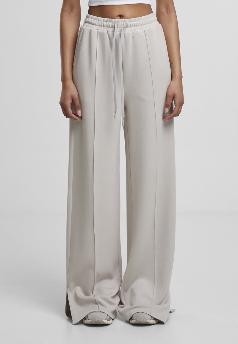 Pantalon de survêtement large et gris clair avec une taille élastique et un cordon de serrage, présentant une texture lisse et des coutures latérales.