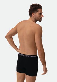 Černé boxerky s šedým elastickým pasem s nápisem "ENDURANCE". Model zobrazen zezadu, s krátkými vlasy a neutrálním pozadím.
