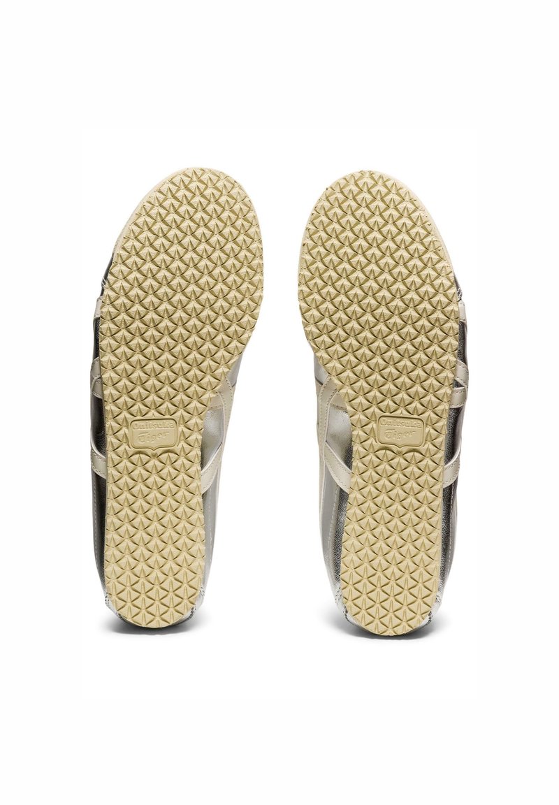 Chaussures de sport légères avec une semelle crème texturée, ornées d'accents métalliques argentés et noirs. Partie supérieure lisse avec un motif géométrique sur le côté.