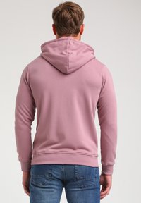 Hætte sweatshirt i lyserød, lavet af blødt stof, med en glat tekstur og ribbede manchetter, parret med mørkeblå jeans.